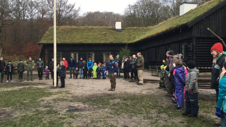 Spejdere i rundkreds omkring flagstang. Person giver besked